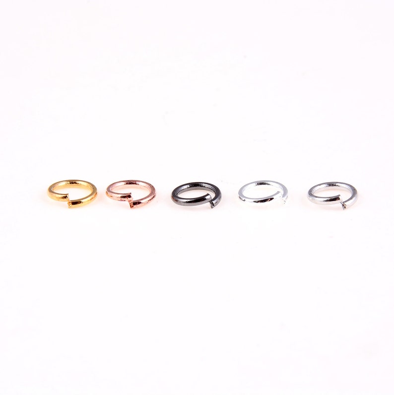 May include: Five jump rings in different colors: gold, rose gold, black, silver, and gunmetal. The rings are all the same size and are arranged in a row.