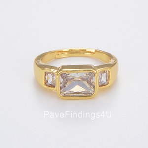 May include: Gold ring with three clear cubic zirconia stones. The center stone is rectangular and the two side stones are smaller and square.