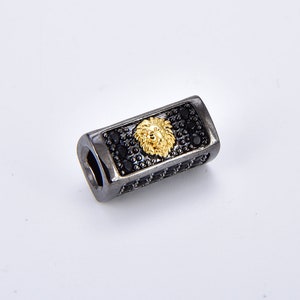 May include: A black metal bead with a gold lion head design and black accents. The bead is approximately 1 inch long.