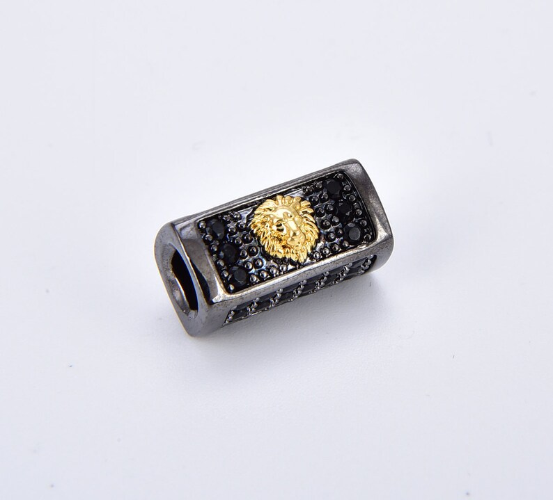 May include: A black metal bead with a gold lion head design and black accents. The bead is approximately 1 inch long.
