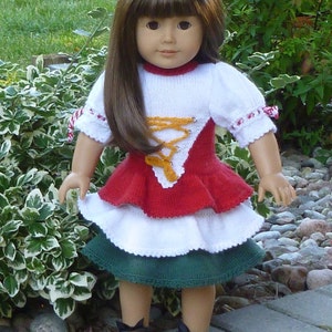 May include: A doll wearing a red, white and green knitted dress with a lace-up bodice. The doll has brown hair and brown eyes.