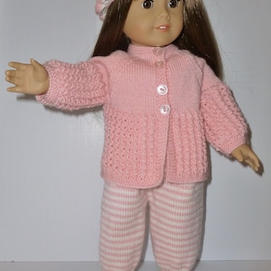 May include: A pink knitted doll outfit with a white striped pattern. The outfit includes a cardigan, trousers, and shoes. The doll is wearing a pink and white hat.