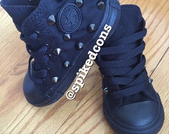 May include: A pair of black high-top Converse sneakers with silver studs. The sneakers are laced up and have a black rubber sole.