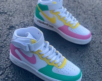 May include: A pair of white high-top sneakers with a green, yellow, and pink color block design. The Nike swoosh logo is yellow on one shoe and pink on the other.