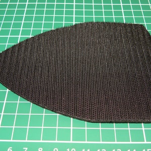 May include: A black sanding pad with a hook and loop backing. The pad is designed for use with a sander.