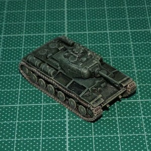 May include: A green toy tank with a detailed design, featuring a turret and tracks. The tank is sitting on a green cutting mat.