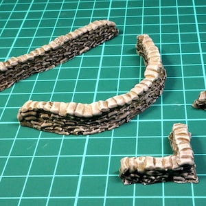Puede incluir: Cuatro piezas de un kit de maqueta de muro de piedra marrón. Las piezas son curvas y rectas, y se pueden usar para crear una variedad de diseños de muros.