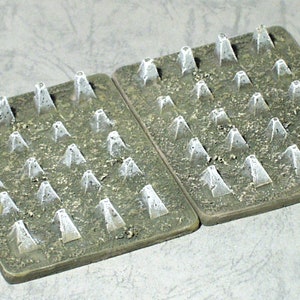 May include: Two green square-shaped bases with rows of white plastic cones, resembling a field of miniature obstacles.