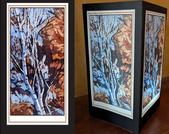 May include: A black, three-sided decorative lantern featuring a watercolor painting of a tree scene. The artwork depicts white tree trunks against a backdrop of blue sky and brown foliage. The lantern has a white border with a gold trim.