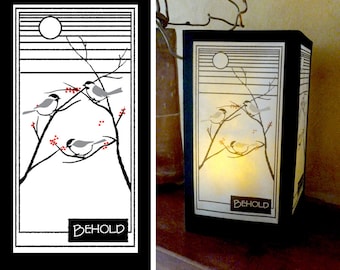 May include: A black framed lantern with a white background and a black and white illustration of birds on branches with red berries. The lantern has a white background with the word "BEHOLD" printed in black at the bottom.