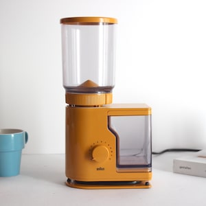 Peut inclure: Un moulin à café en plastique jaune et transparent avec un bac à grains transparent et un récipient transparent pour le café moulu. Le moulin possède un bouton pour régler la grosseur de la mouture.