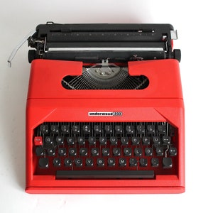 Puede incluir: Una máquina de escribir vintage Underwood 223 roja con un teclado negro y una palanca de retorno de carro negra.