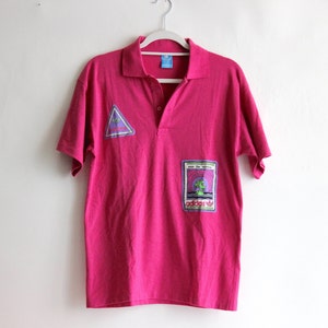 May include: A pink short-sleeved polo shirt with a triangular logo and a rectangular patch with the word "adidas" on it.