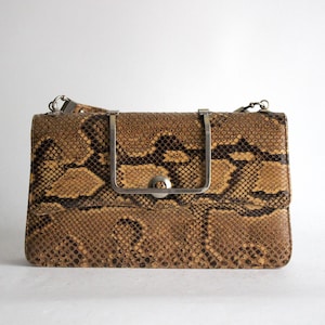 Può includere: Una borsa a mano in pelle di serpente marrone con una chiusura in argento e una tracolla a catena argentata.