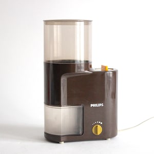 May include: A brown and beige vintage Philips coffee grinder with a clear plastic bean hopper and a yellow control knob.