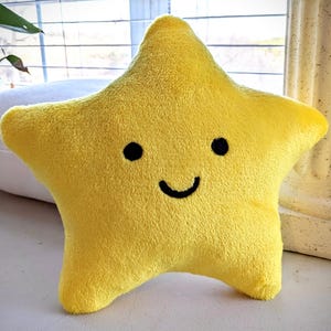May include: A yellow plush star-shaped pillow with a smiling face. The pillow is soft and cuddly, perfect for a child's bedroom.