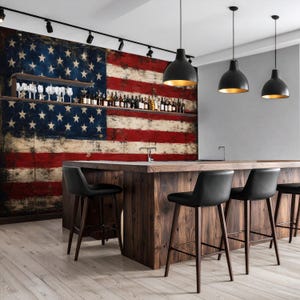 May include: A kitchen island with a dark wood finish and four black bar stools. Behind the island, a wall features a large, weathered American flag mural. A long shelf holds various glass bottles and stemware under black track lighting.