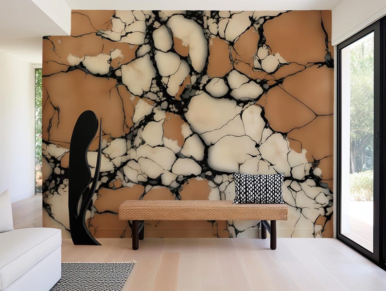 K&ouml;nnte beinhalten: Ein Wandbild mit einem gro&szlig;fl&auml;chigen Risssteinmuster in Beige-, Creme- und Schwarzt&ouml;nen. Eine rechteckige geflochtene Bank mit einem schwarz-wei&szlig; gemusterten Kissen steht vor der Wand, neben einer hohen, schwarzen, abstrakten Skulptur.