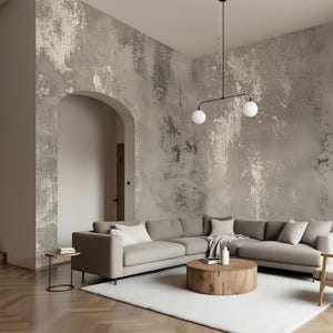 May include: A modern living room with a large sectional sofa in a neutral color, a wooden coffee table, and a white rug. The walls have a textured, distressed finish. A staircase and arched doorway are visible.