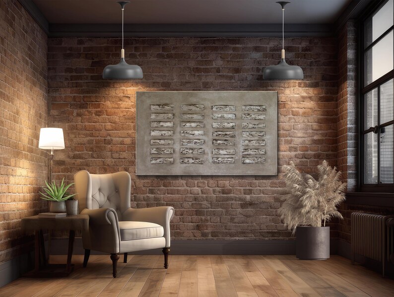 Op de afbeelding: Een grijze en witte abstracte kunstprint met een geometrisch patroon hangt aan een bakstenen muur in een woonkamer. De print is ingelijst en wordt verlicht door twee grijze hanglampen. Een grijze fauteuil staat in de hoek van de kamer, en een potplant staat in de hoek van de kamer.