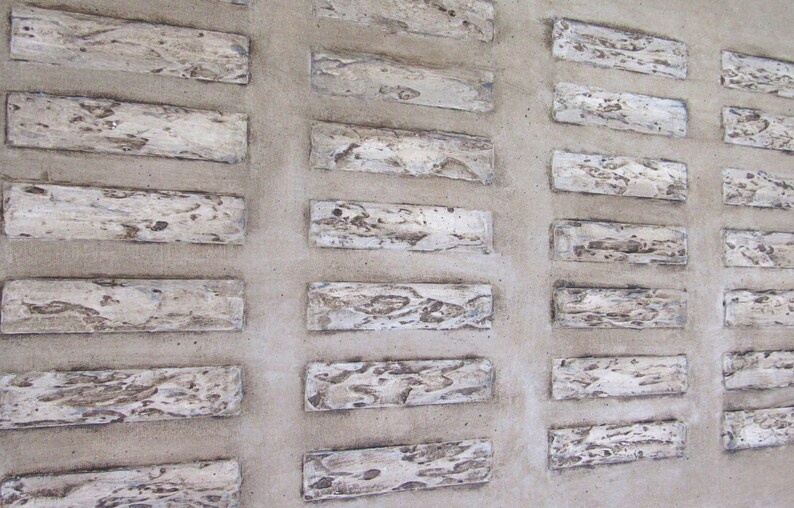 Op de afbeelding: Een close-up van een muur met een patroon van rechthoekige tegels. De tegels zijn gemaakt van een lichtgekleurd materiaal, mogelijk steen of beton, en hebben een ruw, getextureerd oppervlak. De tegels zijn gerangschikt in een rasterpatroon, waarbij elke tegel iets verschoven is ten opzichte van de volgende.