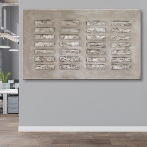 Op de afbeelding: Abstracte wandkunst met een rechthoekig canvas met een textuur, lichtgrijze achtergrond. Het canvas is verdeeld in drie secties, elk met een reeks horizontale, rechthoekige vormen in een lichtere tint grijs.