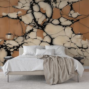 K&ouml;nnte beinhalten: Ein Schlafzimmer mit einem Bett mit wei&szlig;er Bettw&auml;sche und einer beigen Tagesdecke, das vor einer Wand mit einer Tapete mit gro&szlig;fl&auml;chigem, rissigem Steinmuster in Beige-, Creme- und Schwarzt&ouml;nen steht, flankiert von zwei h&auml;ngenden Pendelleuchten.