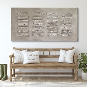Op de afbeelding: Een rechthoekig abstract schilderij met een grijze achtergrond en witte lijnen. Het schilderij hangt aan een witte muur boven een houten bank met twee kussens. De kussens zijn wit met zwarte tekst die "welcome home" luidt.