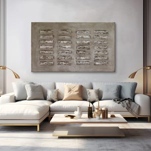 Op de afbeelding: Een groot abstract schilderij met een textuurrijke, grijze achtergrond en een patroon van rechthoekige vormen in grijstinten en wit. Het schilderij hangt aan een muur boven een witte hoekbank met kussens en een salontafel.