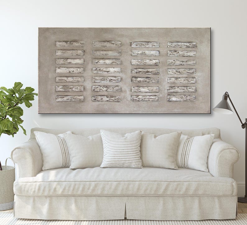 Op de afbeelding: Een groot abstract schilderij met een grijze achtergrond en een patroon van witte rechthoekige vormen. Het schilderij hangt boven een witte bank met kussens.