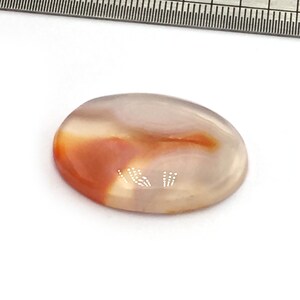 May include: A smooth, oval-shaped agate stone with a white, gray, and orange color pattern.