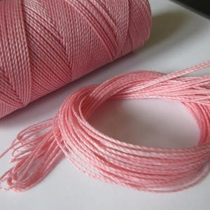 Könnte beinhalten: Eine Spule mit rosa gewachstem Baumwollgarn. Das Garn ist fest um die Spule gewickelt und bereit für Bastelarbeiten.