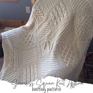 May include: A white knitted throw blanket with a square knit pattern. The blanket is draped over a chair and has a textured design.