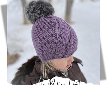 May include: Purple knitted hat with a cable knit pattern and a faux fur pom pom. The hat is worn by a child in a snowy outdoor setting. Winter Bliss Hat knitting pattern.