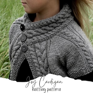 Könnte beinhalten: Ein grauer Strickcardigan mit einem Zopfmuster und drei schwarzen Knöpfen. Der Cardigan hat einen breiten Kragen und ist vorne offen. Der Text "Joy Cardigan knitting pattern" ist in Weiß auf weißem Hintergrund geschrieben.