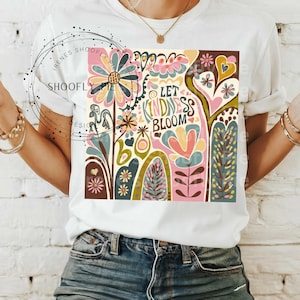 May include: White t-shirt with a colorful graphic design featuring flowers, hearts, and the text "Let Kindness Bloom".