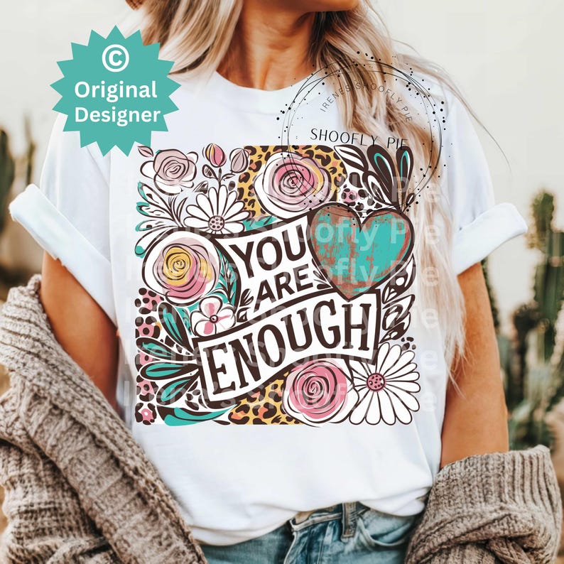 May include: White t-shirt with a floral design and the text "You Are Enough" in black lettering. The design includes a turquoise heart with a distressed look.