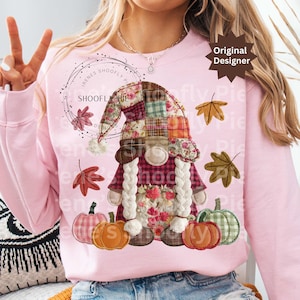 Op de afbeelding: Zachtroze sweatshirt met een herfstkabouterontwerp. De kabouter heeft een patchwork hoed, bloemendetails en een gevlochten witte baard. Pompoenen en bladeren zijn ook afgebeeld. De tekst "SHOOFY PIE" is zichtbaar.