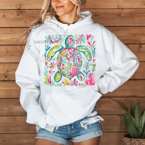 May include: White hoodie with a colorful floral design featuring a sea turtle. The design includes pink, yellow, green, and blue flowers.