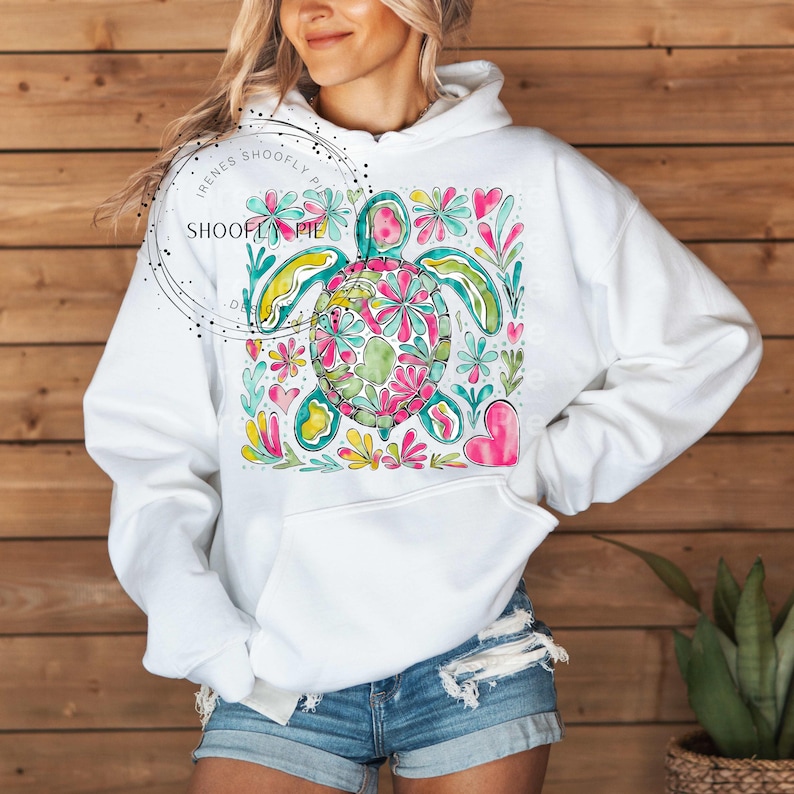 May include: White hoodie with a colorful floral design featuring a sea turtle. The design includes pink, yellow, green, and blue flowers.