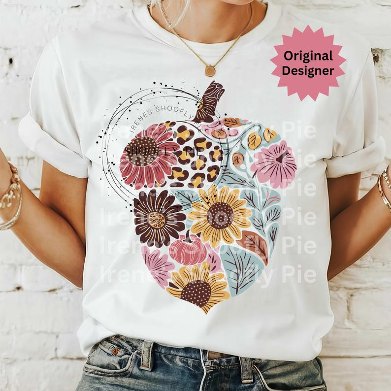 May include: White t-shirt featuring a floral pumpkin design. The pumpkin is composed of sunflowers, pink flowers, and a leopard print section. The text "Irenes Shoofly Pie" is in a circle around the pumpkin.