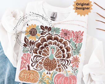 May include: White sweatshirt featuring a colorful Thanksgiving-themed design. The design includes a turkey with a leopard print pattern, pumpkins, and floral elements. The text "Original Designer" is visible on the top right.