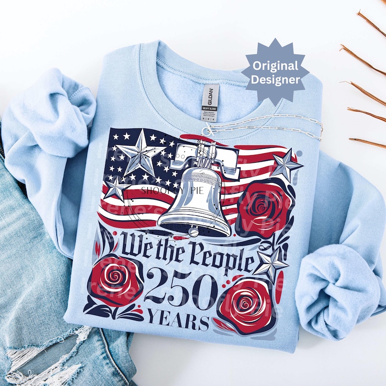 K&ouml;nnte beinhalten: Hellblaues Sweatshirt mit patriotischem Design. Es zeigt die amerikanische Flagge, die Freiheitsglocke und rote Rosen. Der Text lautet "We the People 250 Years". Das Design beinhaltet Sterne und Streifen.