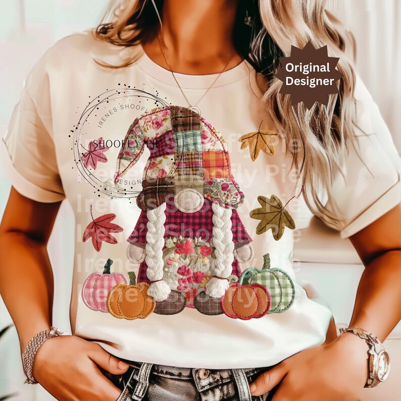 Peut inclure: T-shirt cr&egrave;me avec un motif de gnome patchwork avec des tresses, un chapeau &agrave; carreaux et des d&eacute;tails floraux. Le motif comprend des citrouilles et des feuilles d'automne. Le texte "Irenes Shoofly Pie Design" est &eacute;galement visible.