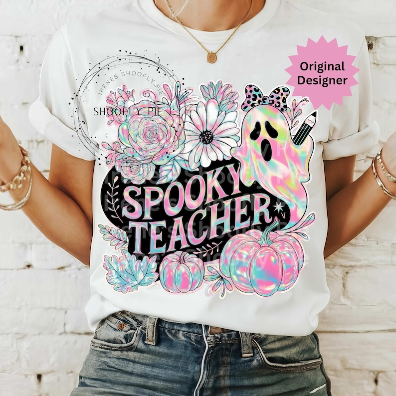 May include: White t-shirt with a colorful "Spooky Teacher" graphic. The design features a ghost, pumpkins, flowers, and the text "Spooky Teacher". The ghost has a bow and pencil. The shirt has rolled-up sleeves.