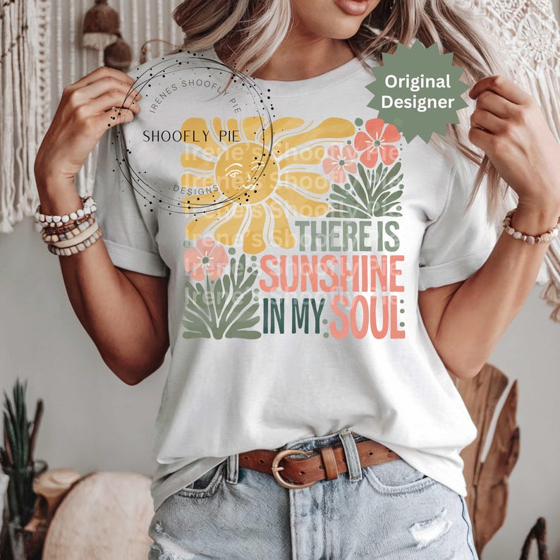 May include: White t-shirt with a floral and sun design. The design includes the text "THERE IS SUNSHINE IN MY SOUL" in various colors. The shirt has short sleeves and a crew neck.