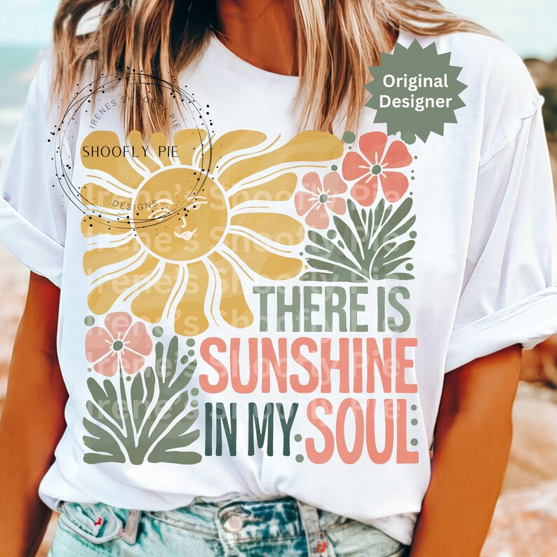 May include: White t-shirt with a colorful graphic design. The design features a yellow sun, pink flowers, and the text "THERE IS SUNSHINE IN MY SOUL" in coral and green. A casual, comfortable tee.