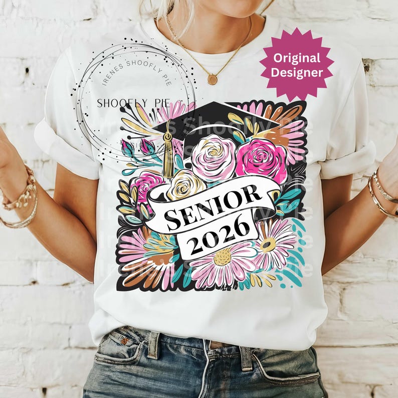 以下が含まれることがあります： 卒業キャップ、バラ、デイジーなどの花柄が特徴の白いTシャツ。「SENIOR 2026」の文字がバナーに表示されています。シャツは袖をまくり、丸いネックラインになっています。