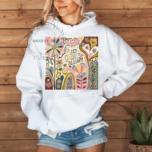 May include: White hoodie with a colorful floral design and the text "Let Kindness Bloom".