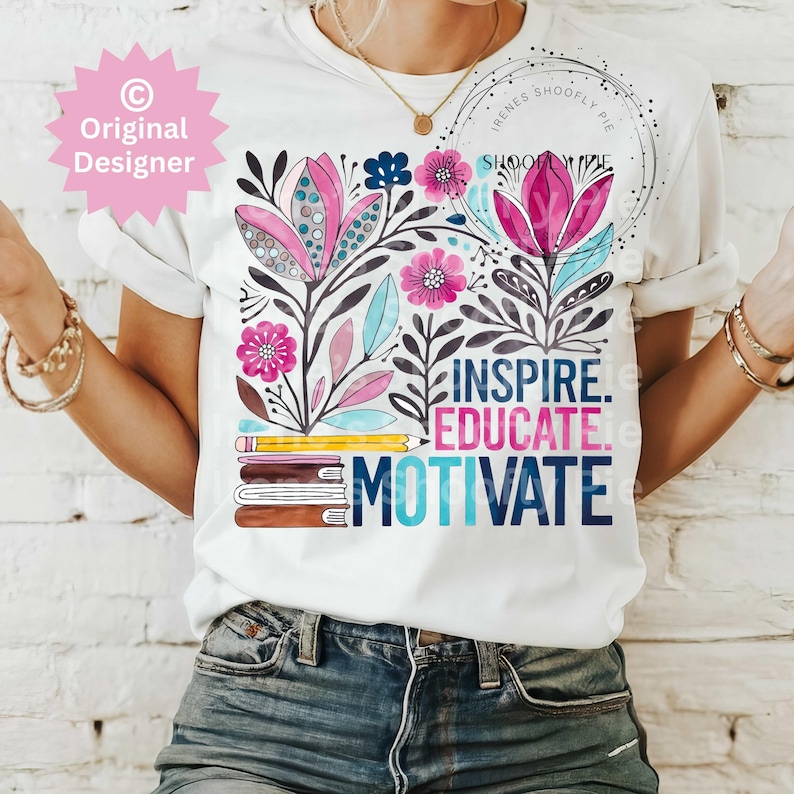 Op de afbeelding: Wit T-shirt met een bloemenontwerp in roze, blauw en zwart. Het shirt heeft de woorden "INSPIRE. EDUCATE. MOTIVATE." in een kleurrijk lettertype, samen met een potlood- en boekenafbeelding. Het ontwerp bevat de tekst "Original Designer" en "Irenes Shoofly Pie."